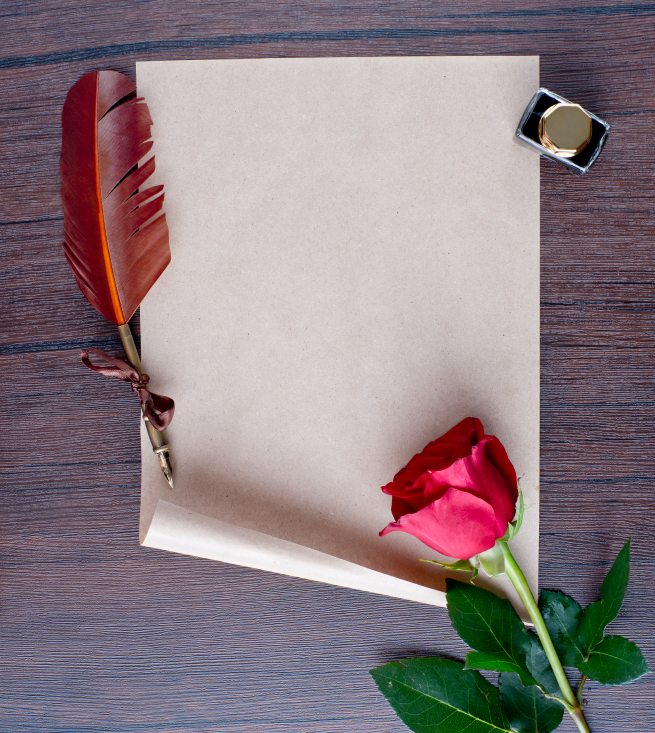 pen and old paper with a rose on a wooden table